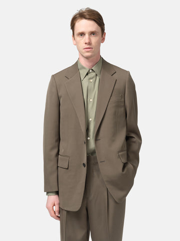 Half-body shot of the Model standing in studio wearing the AURALEE Light Wool Max Gabardine Jacket Dark in Olive Brown