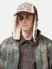 Close-up view of model wearing the KAPITAL DENIM REPAIR SERVICE LUMBER Trucker Cap ECTxBrwn with ear flap down