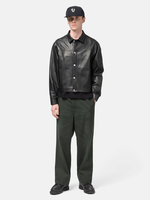 Model standing in studio wearing the UNLIKELY Zero Leather Trucker JKT in Black