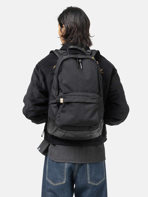 Model wearing the Visvim Cordura 22L backpack in black on the shoulder.